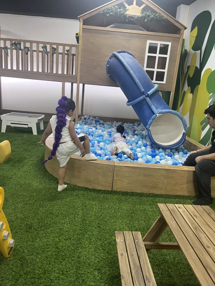 Alberca de pelotas con resbaladilla junto a mesas de madera